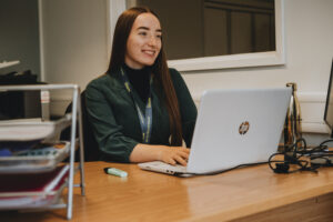 EMA's Jess on laptop, smiling.