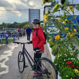 EMA's Mental Health First Aider Julie wearing and red coat and a helmet with a bike about to ride off. For this years World Mental Health Day.