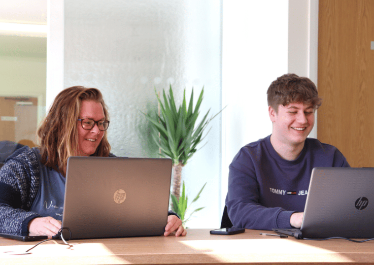 EMA learners working on their laptops, smiling.