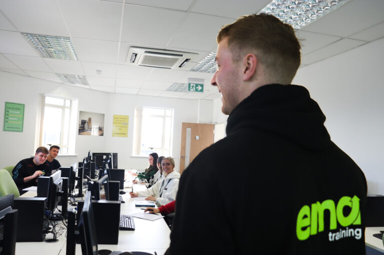 EMA's Content Creator Trainer, Stuart, teaching a class of apprentices. Stuart is facing the class, you can see the EMA green logo on the back of his jumper.