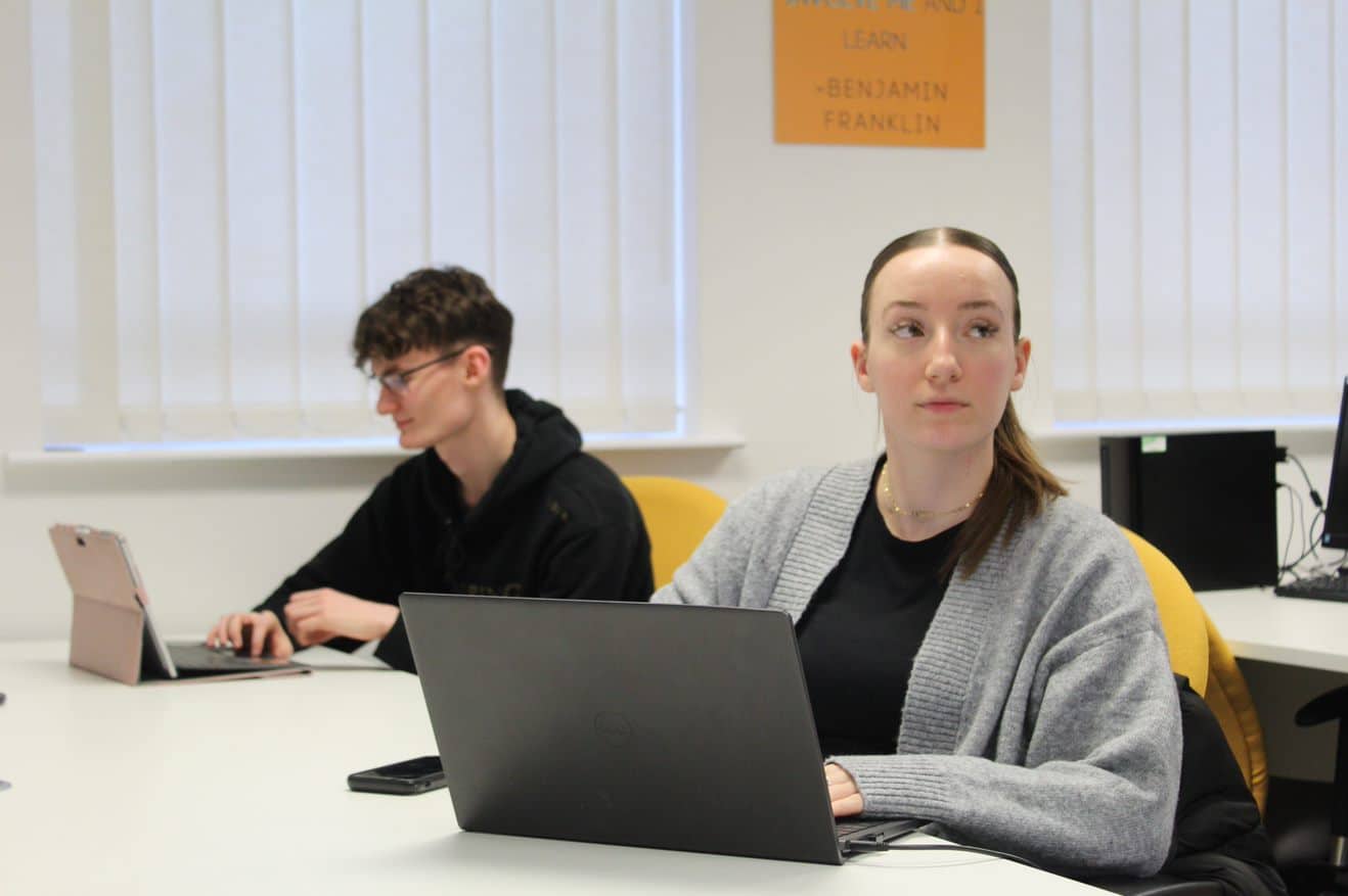 two marketing apprentices, sat working on laptops