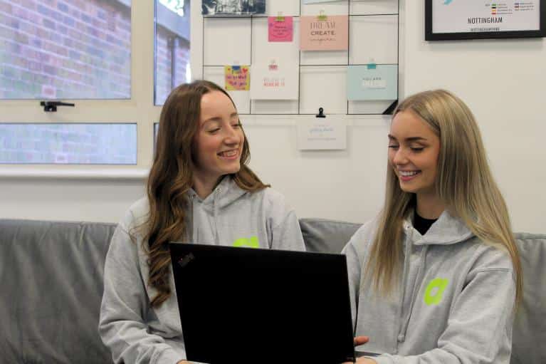 Two young female apprentices smiling on a sofa