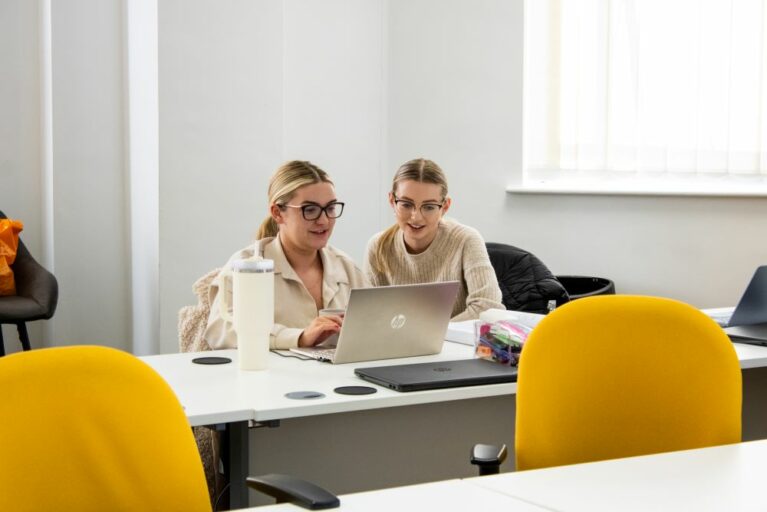 Two female apprentices sat at a laptop smiling