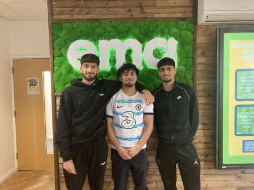 3 apprentices stood as friends in front of a green EMA logo